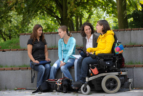 Studierende mit Behinderung Vier Studierende, darunter Studierende mit Behinderung, sitzen gemeinsam auf dem Campus.