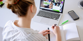Arbeit am Laptop Am Schreibtisch sitzende Studentin arbeitet am Laptop, daneben liegen Bücher und Stifte.